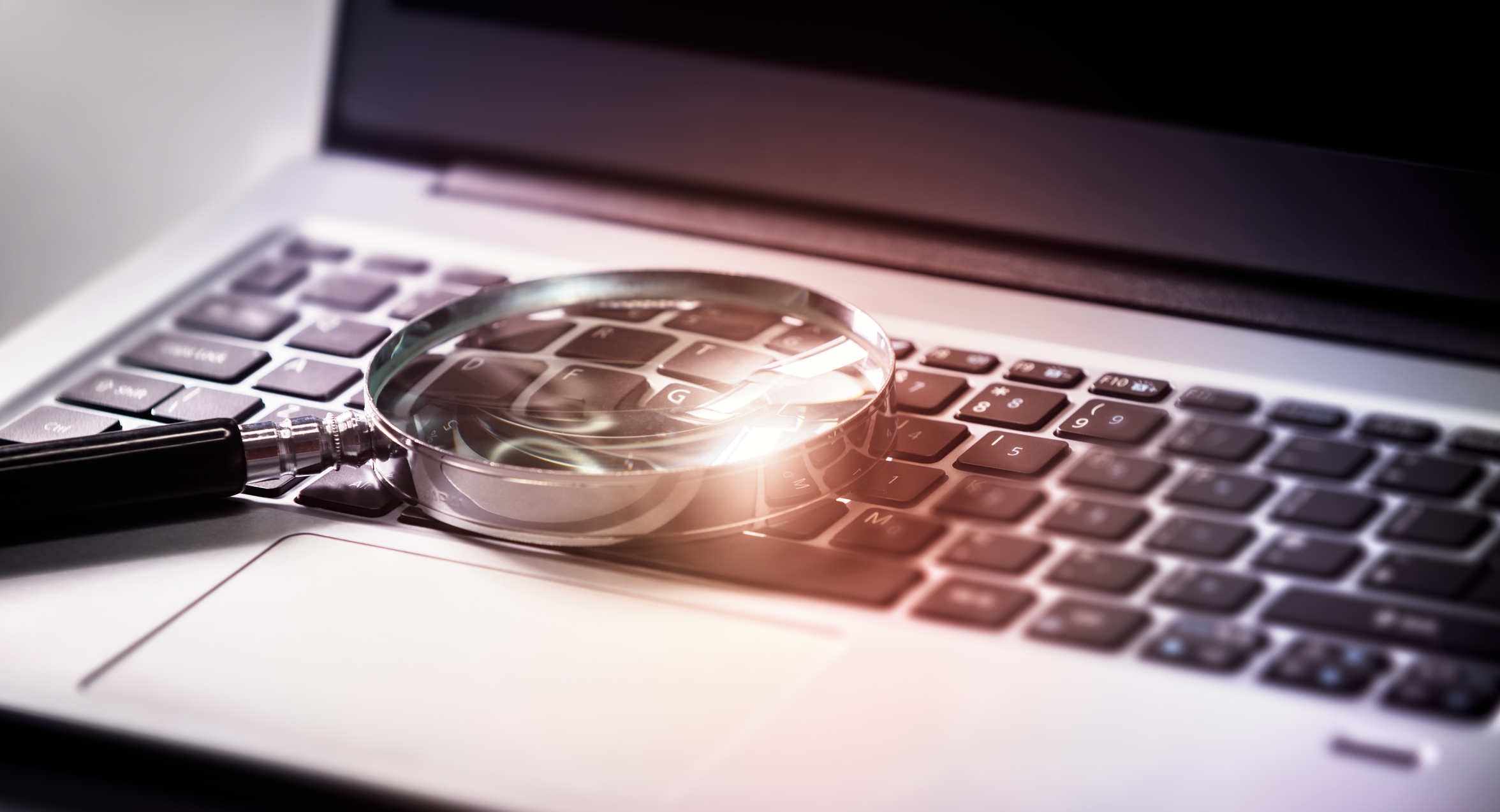Magnifying glass on laptop keyboard searching the internet for online documents